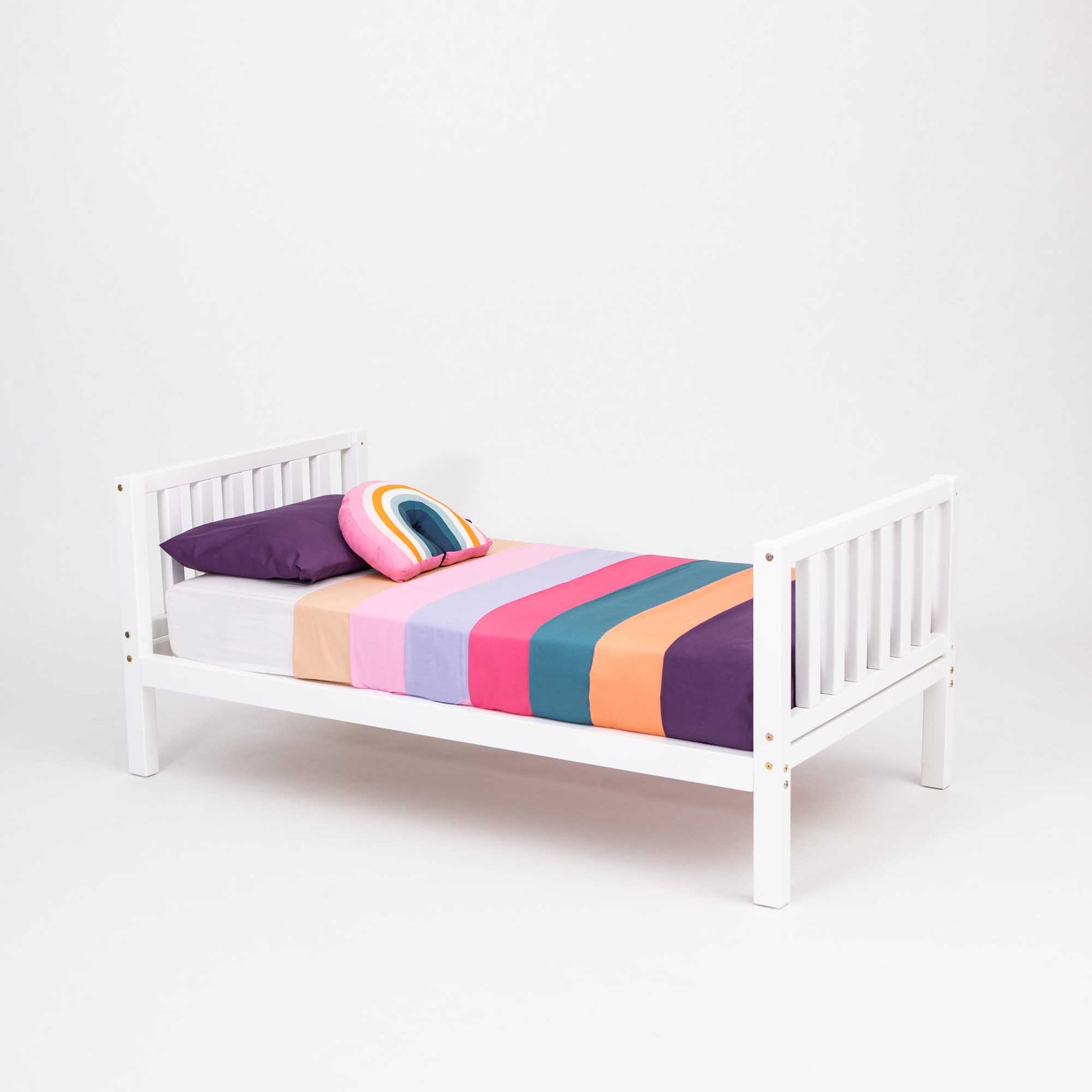 A 2-in-1 kid's bed on legs with a vertical rail headboard and footboard with a colorful striped blanket.