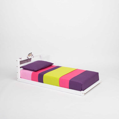 A Sweet Home From Wood toddler floor bed with a horizontal rail headboard, with a purple, pink, and green stripe.