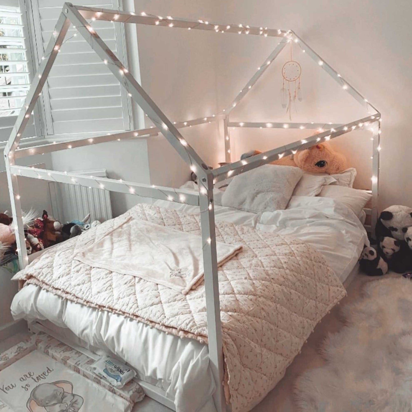 A cozy sleep haven with a teddy bear on a Sweet Home From Wood Montessori Children's house bed with a horizontal headboard featuring gentle lights.