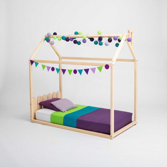 A child's wooden Kids' house-frame bed with a picket fence headboard, designed in a montessori house bed style.