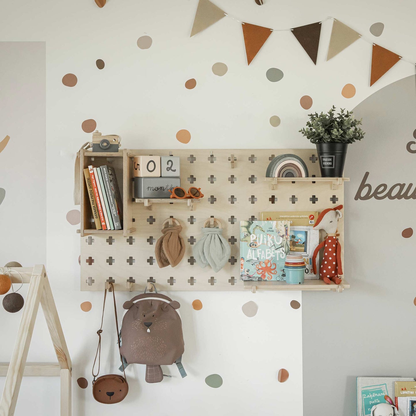 A children's room with wall-mounted, adjustable Floating Shelves Pegboard holding books, toys, and decor. A backpack hangs below the pegboard wall shelf. The wall is decorated with dotted patterns and a triangular flag banner.