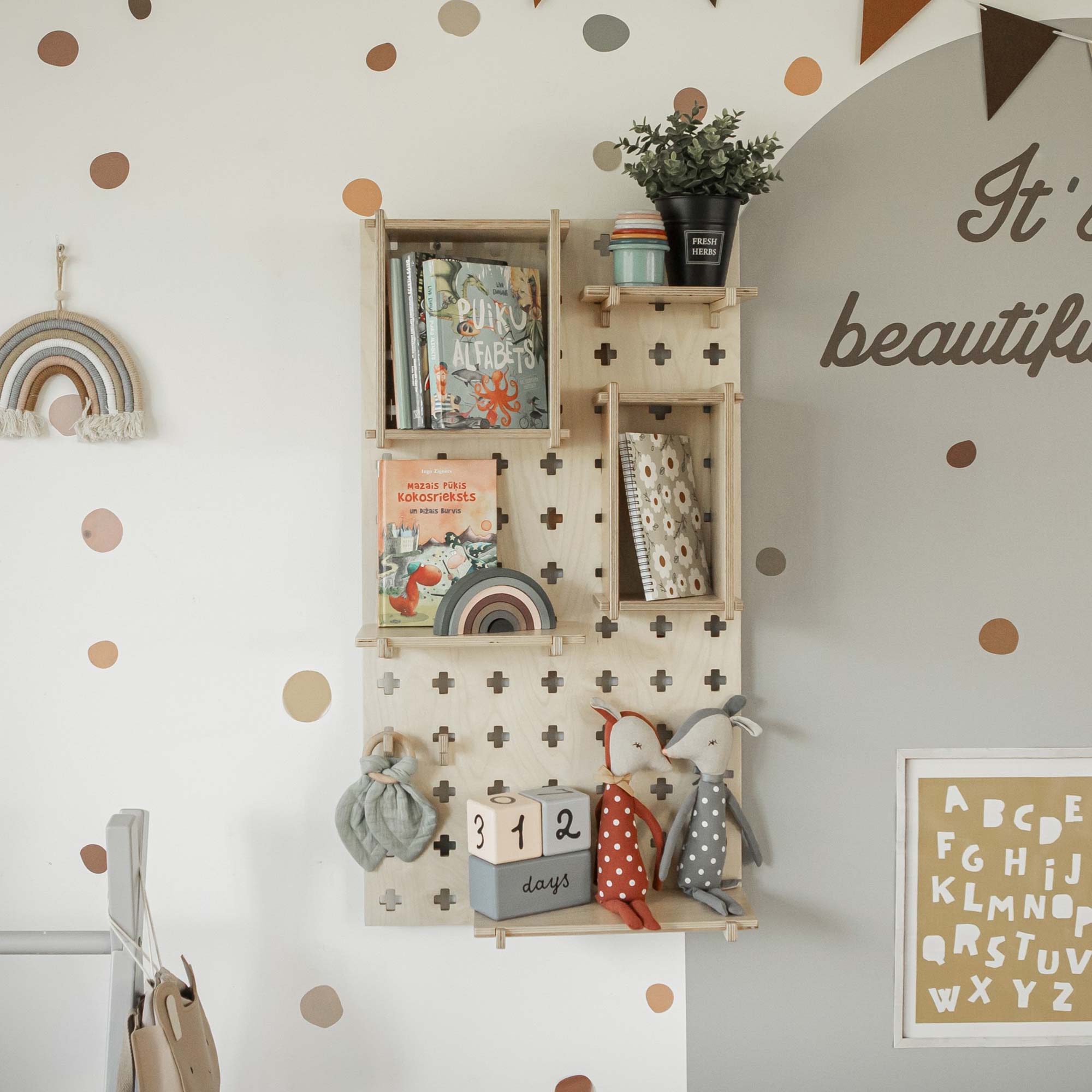 Pegboard Montessori Open Shelf unit adorned with children's books, stuffed animals, a plant, and decorative items. The wall is decorated with polka dots, a rainbow design, and alphabet prints. Sweet Home from Wood presents the ideal storage solution which also includes a "312 days" countdown sign in blocks.