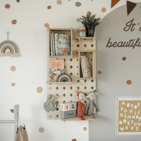Pegboard Montessori Open Shelf unit adorned with children's books, stuffed animals, a plant, and decorative items. The wall is decorated with polka dots, a rainbow design, and alphabet prints. Sweet Home from Wood presents the ideal storage solution which also includes a "312 days" countdown sign in blocks.