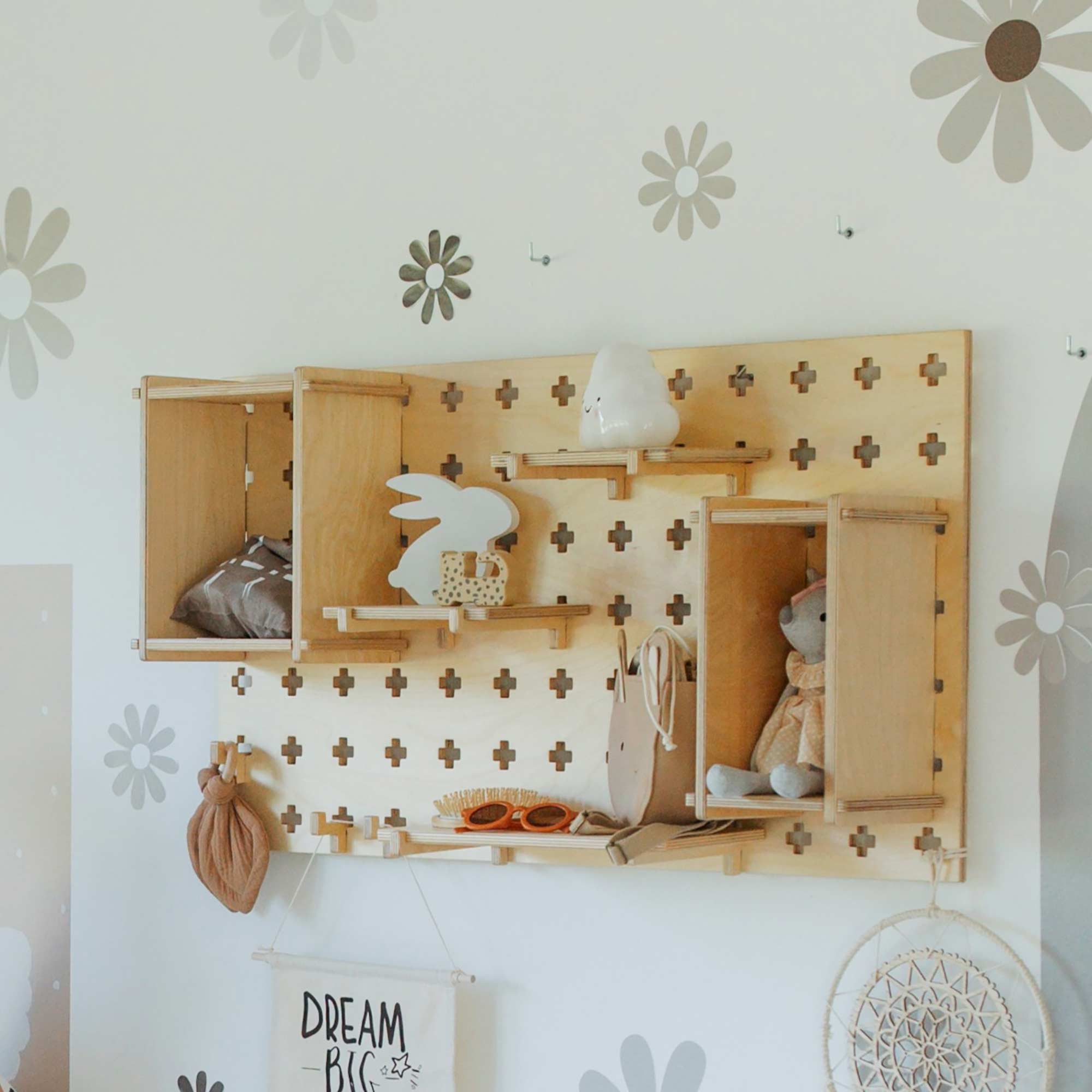 The Pegboard Montessori Open Shelf is organized with a mix of decor items, including a stuffed animal, small bag, ceramic rabbit, and various ornaments, against a wall decorated with flower decals—an elegant storage solution.