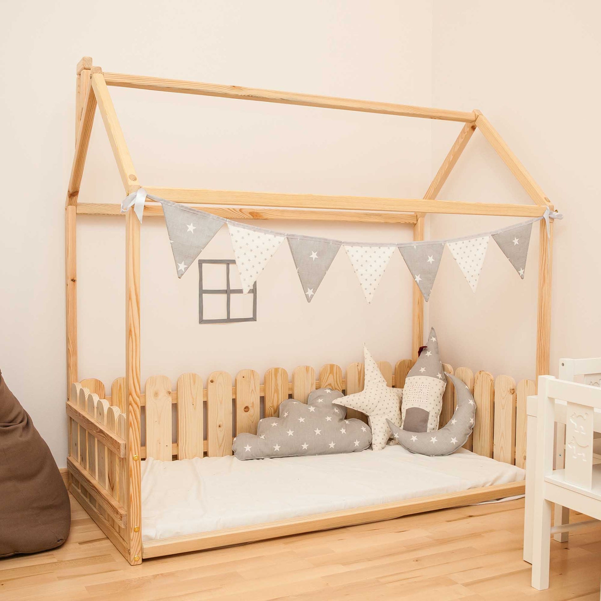 A floor house-frame bed with 3-sided picket fence rails in a child's room.