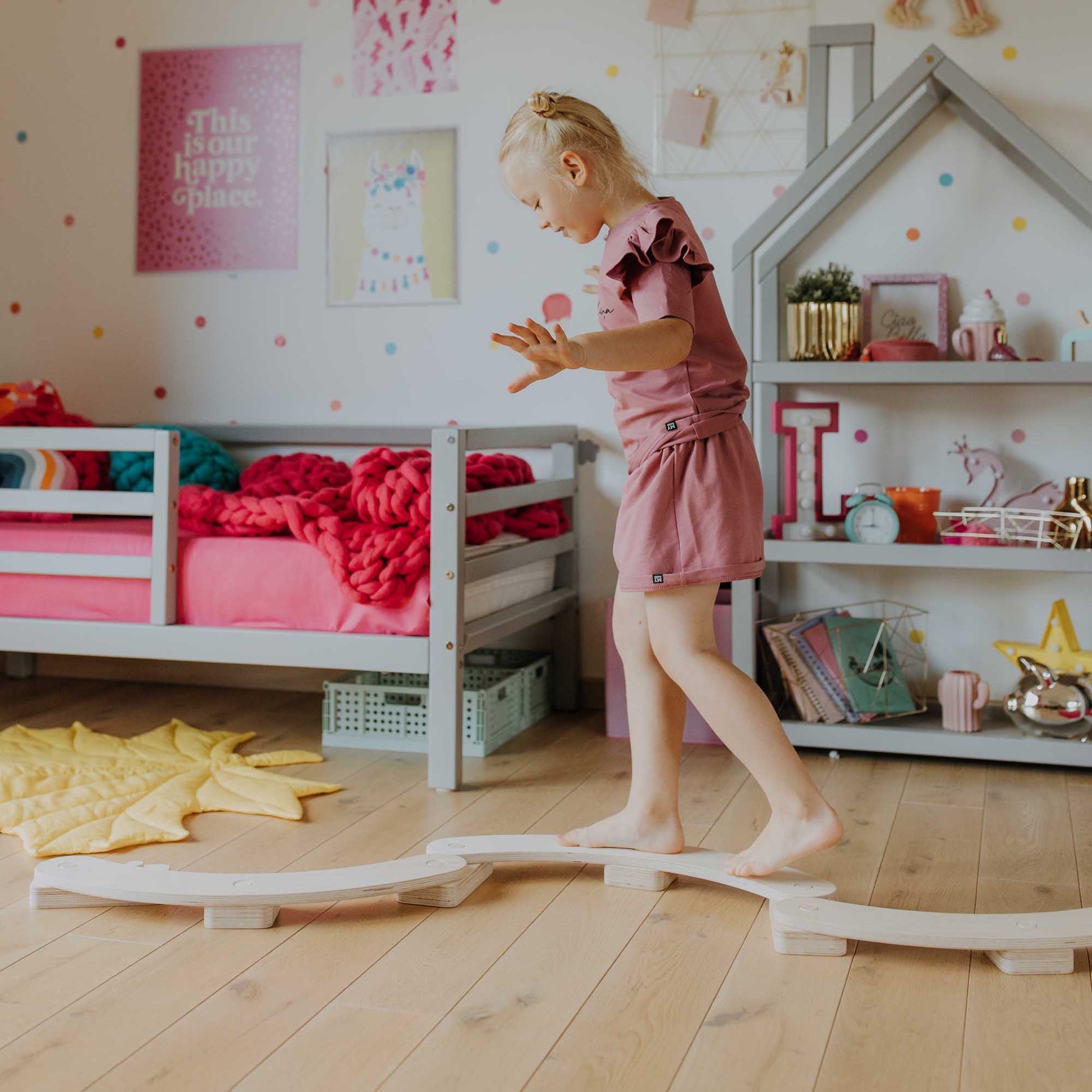 A little girl is standing on a wooden track, exploring her new Round Balance Beams Set gifted for her second birthday.