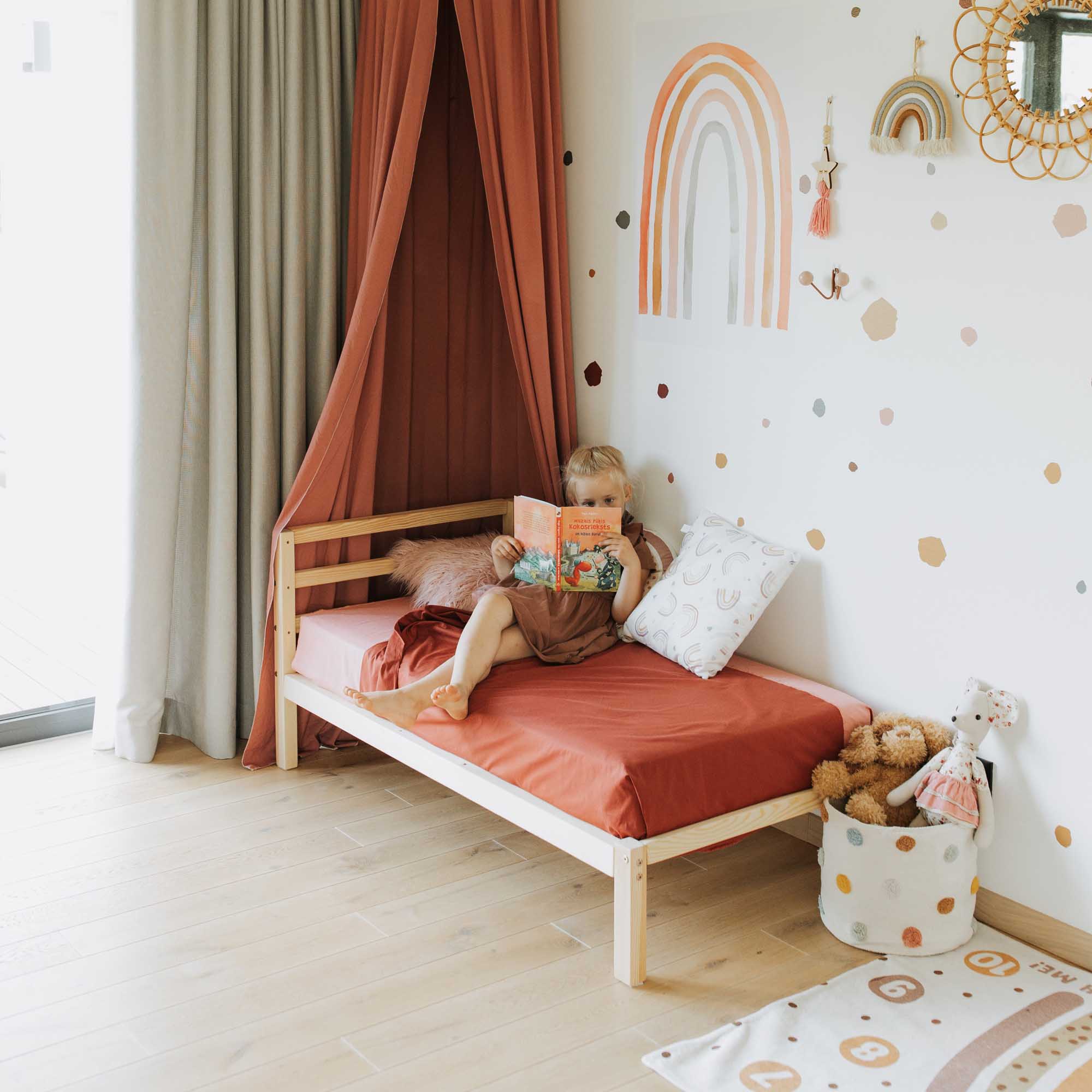 A child's room with a bed and a rainbow wall decal.