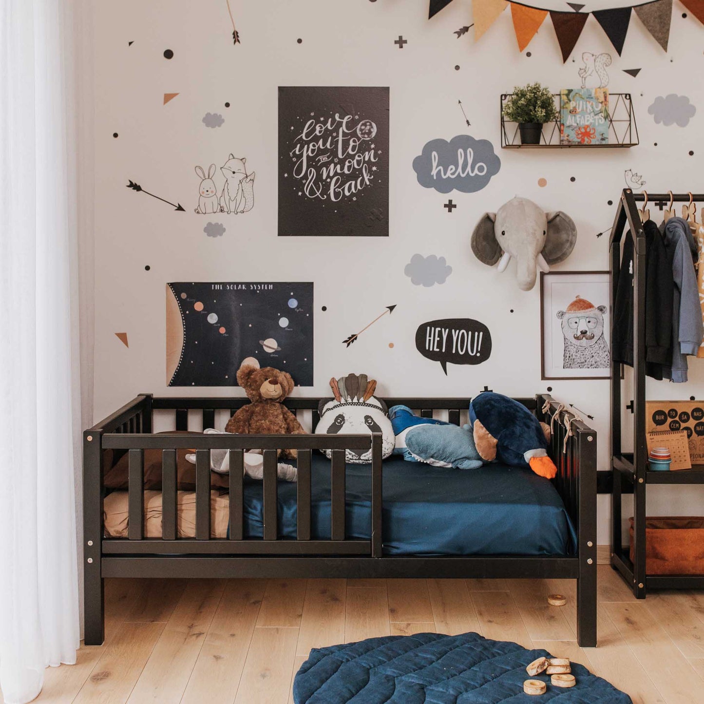A children's room with a Sweet Home From Wood toddler bed on legs with a fence made of solid wood and filled with stuffed animals, allowing for independent sleeping.