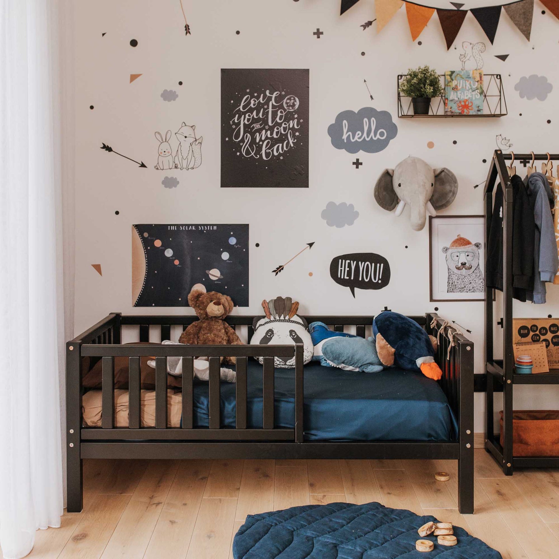 A children's room with a Sweet Home From Wood toddler bed on legs with a fence made of solid wood and filled with stuffed animals, allowing for independent sleeping.