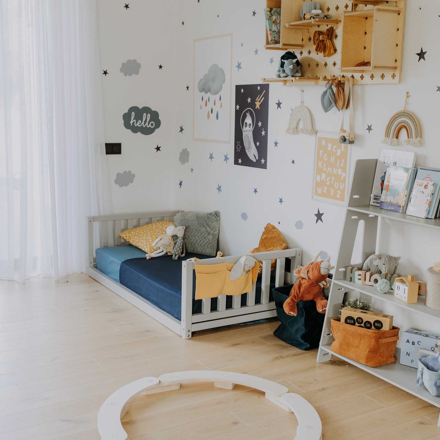 A children's room with a 2-in-1 kid's bed on legs with a vertical rail headboard and footboard, toys, and a circle.