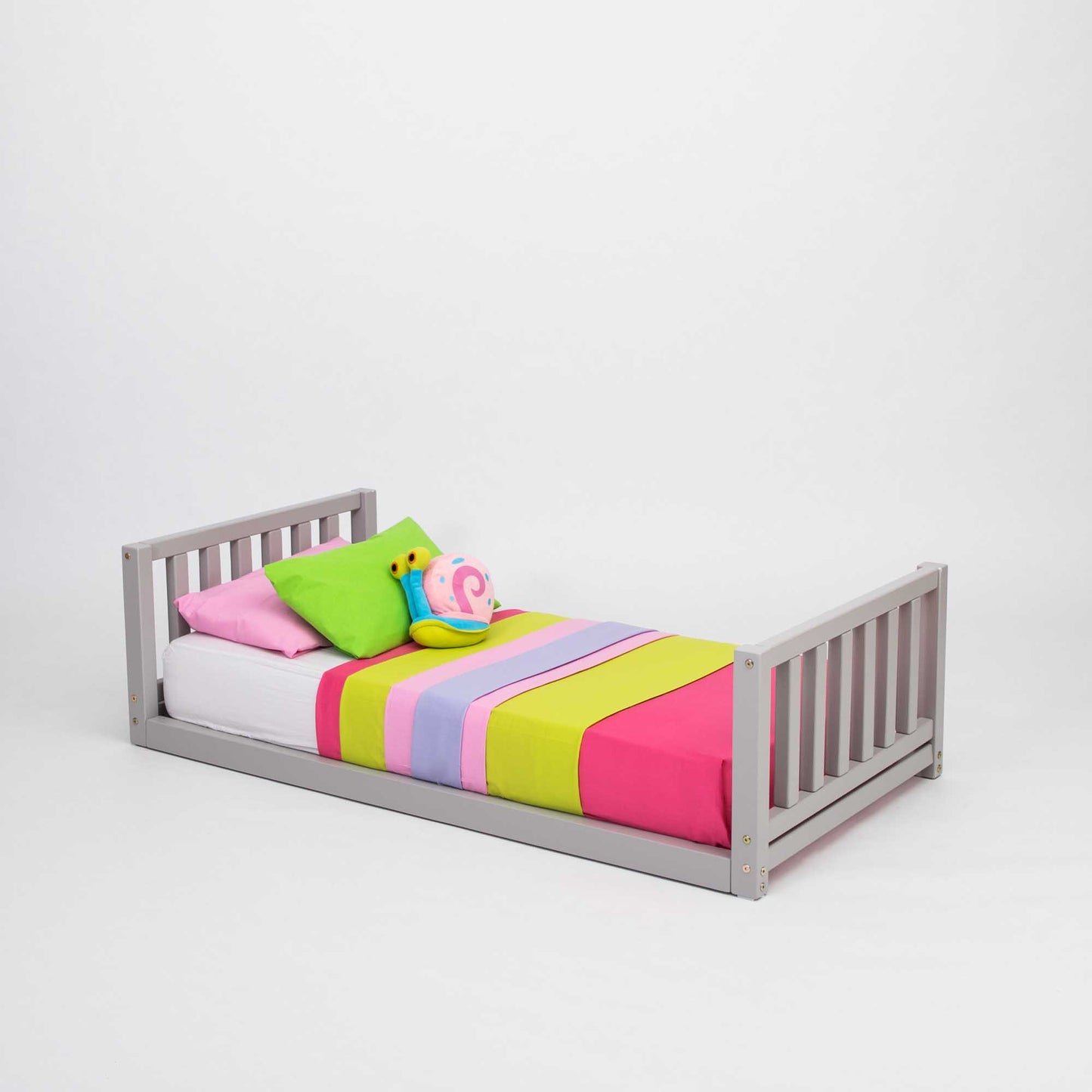 A 2-in-1 kid's bed on legs with a vertical rail headboard and footboard with a colorful blanket on it.