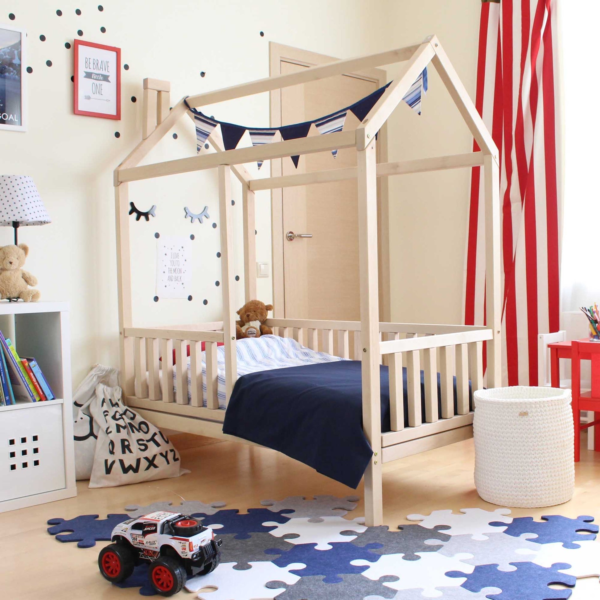 A Kids' house bed on legs with a fence in a child's room with wooden rails.