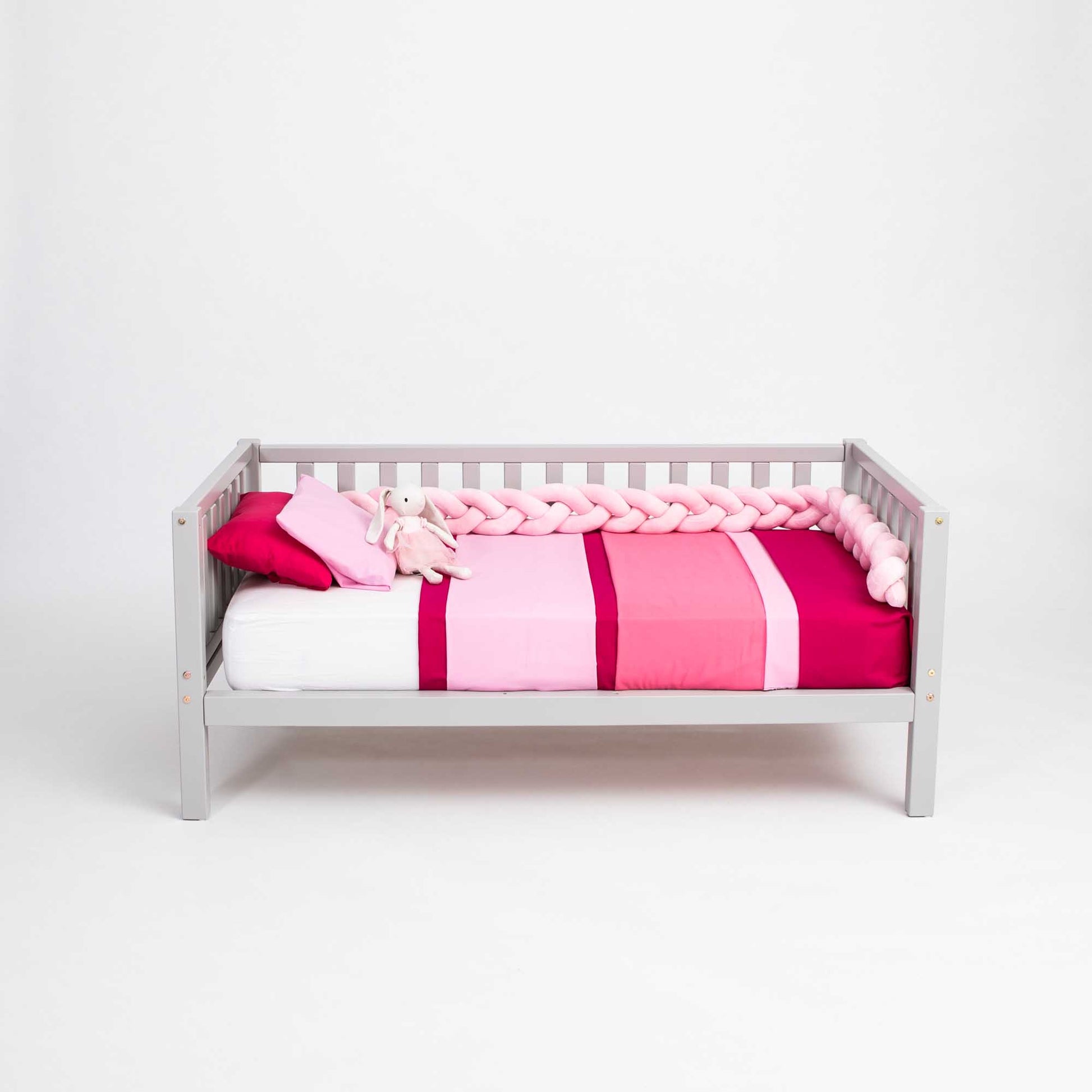 A Kids' platform bed on legs with 3-sided rails from Sweet Home From Wood with a pink blanket.