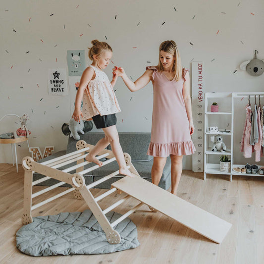 A woman and a little girl playing on a Transformable climbing triangle + Transformable climbing gym + a ramp in a room.