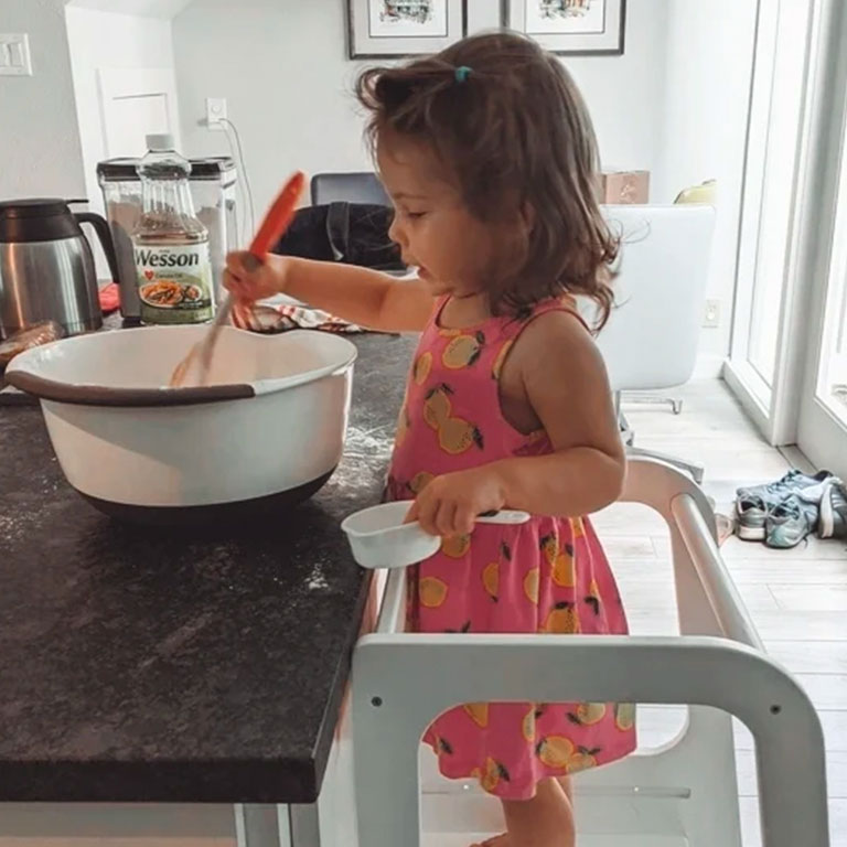 Customer photo of a girl baking and standing on a Montessori step stool.