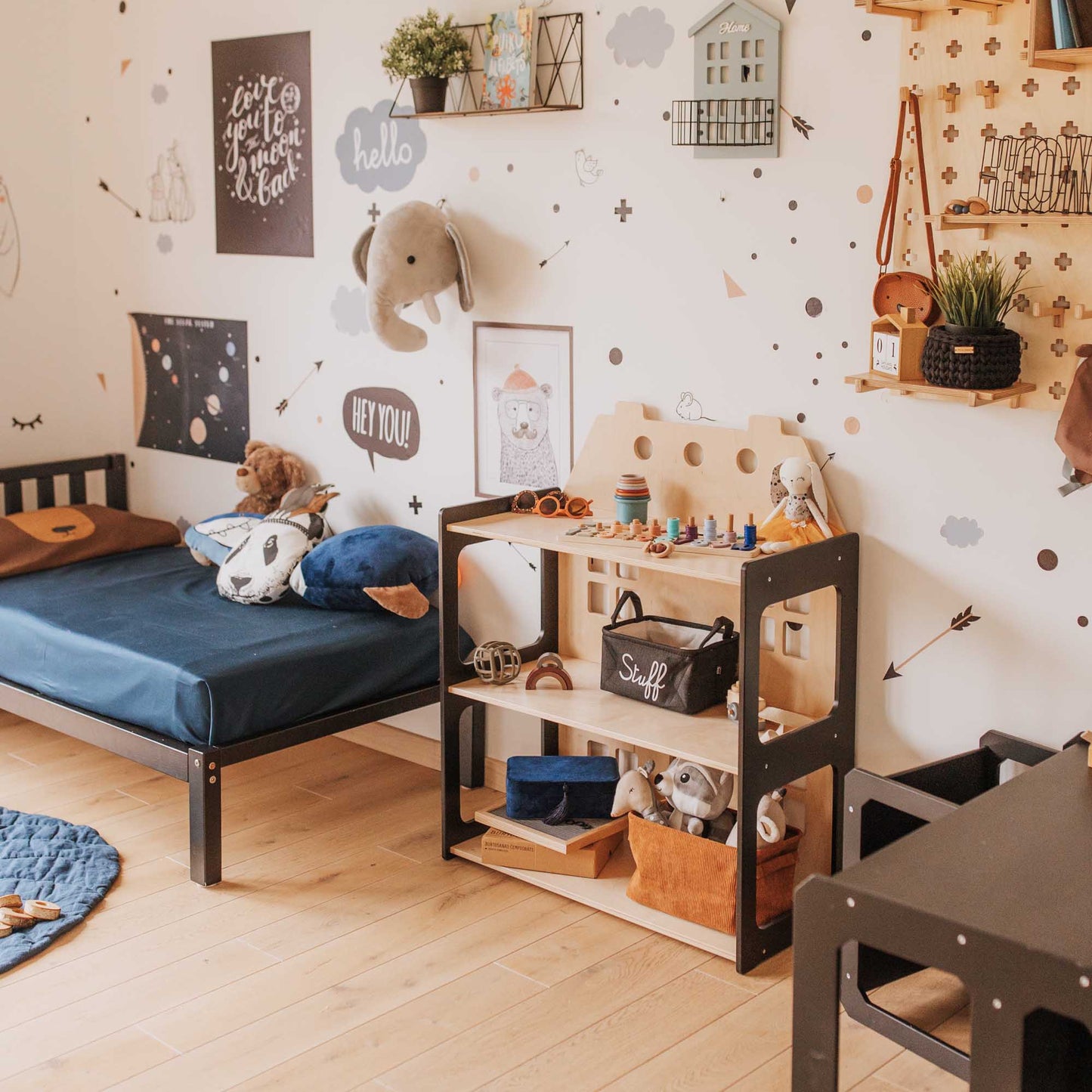 A child's room with a 2-in-1 doll house and Montessori shelf from Sweet Home From Wood, a bed, a desk, and an open toy storage shelf.
