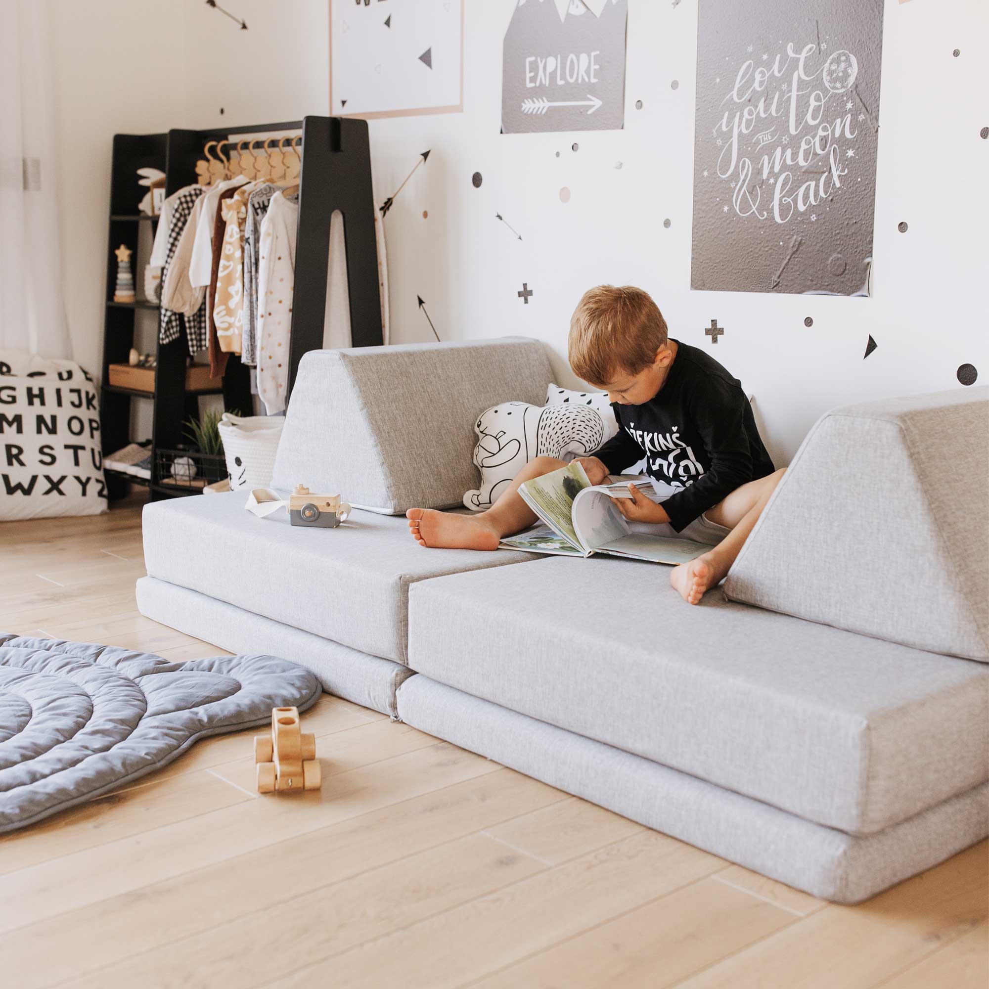 A child is reading a book on a grey couch in a child's room.