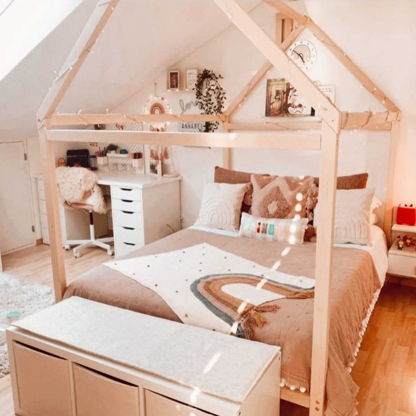 A girl's bedroom featuring a wooden house bed on legs and a desk.