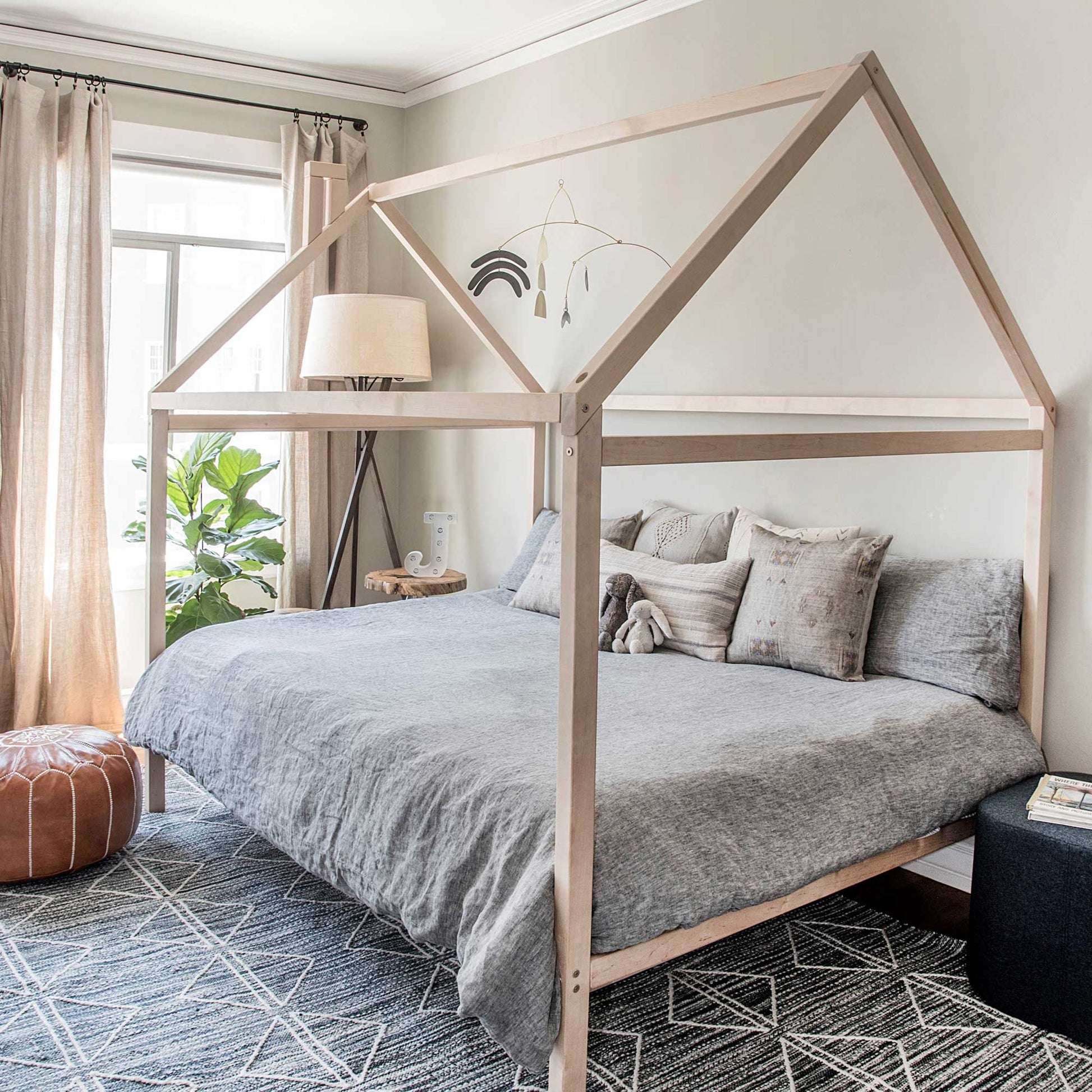 A wooden house bed on legs with a wooden bed frame.