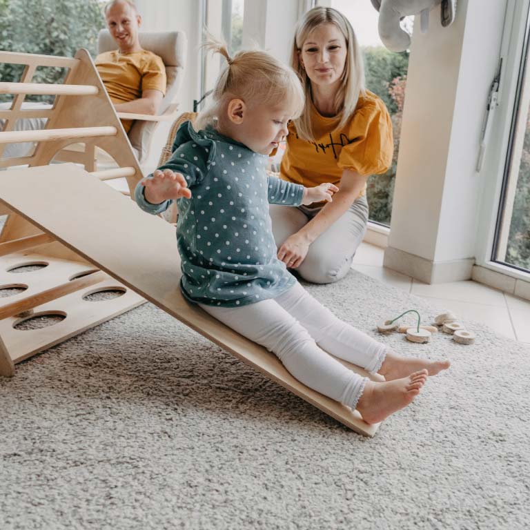 Instagram post of a toddler girl playing on a climbing triangle with a ramp.