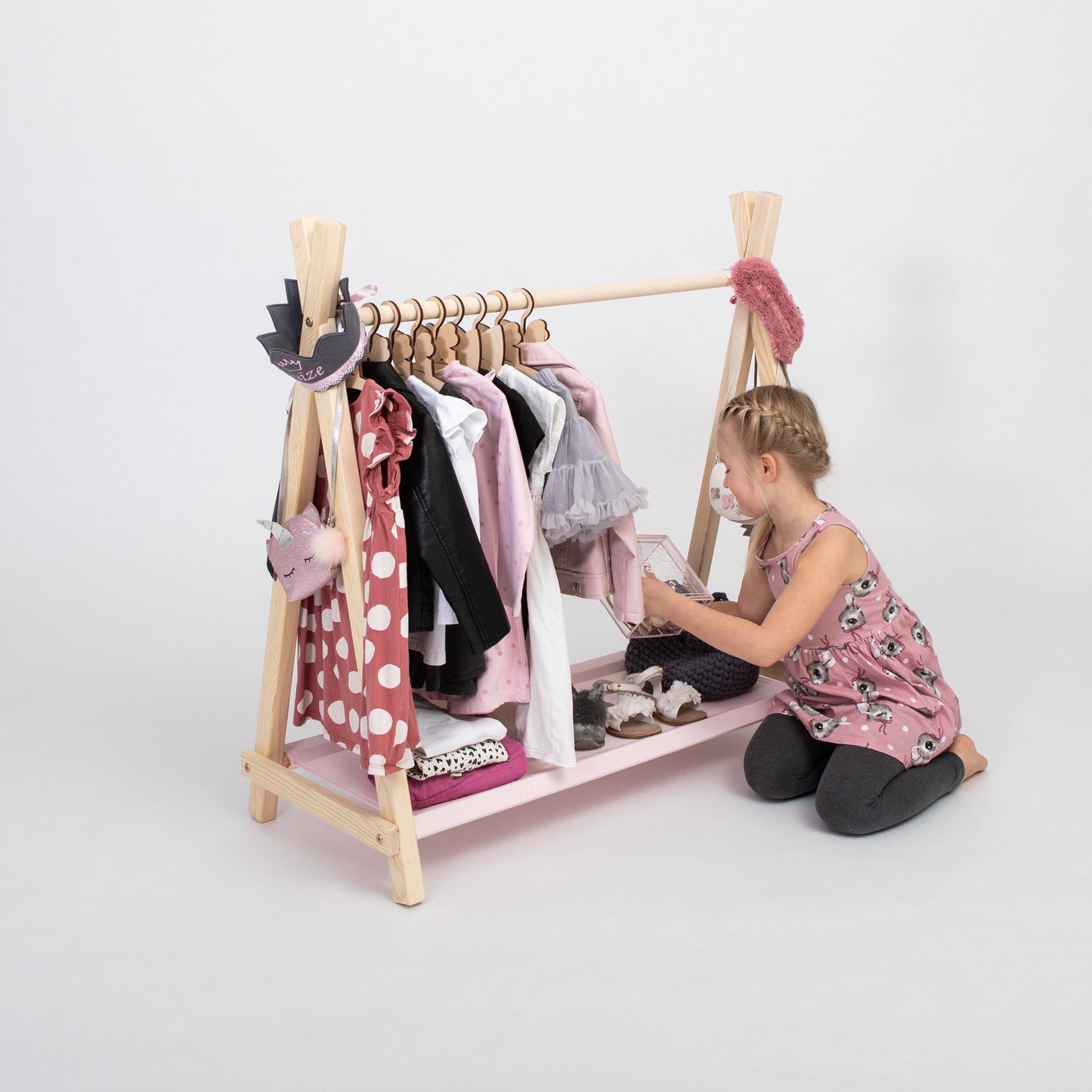 Young girl choosing her clothes on a kid-accessible wooden clothing rack designed for children’s wardrobes and Montessori-style room organization.