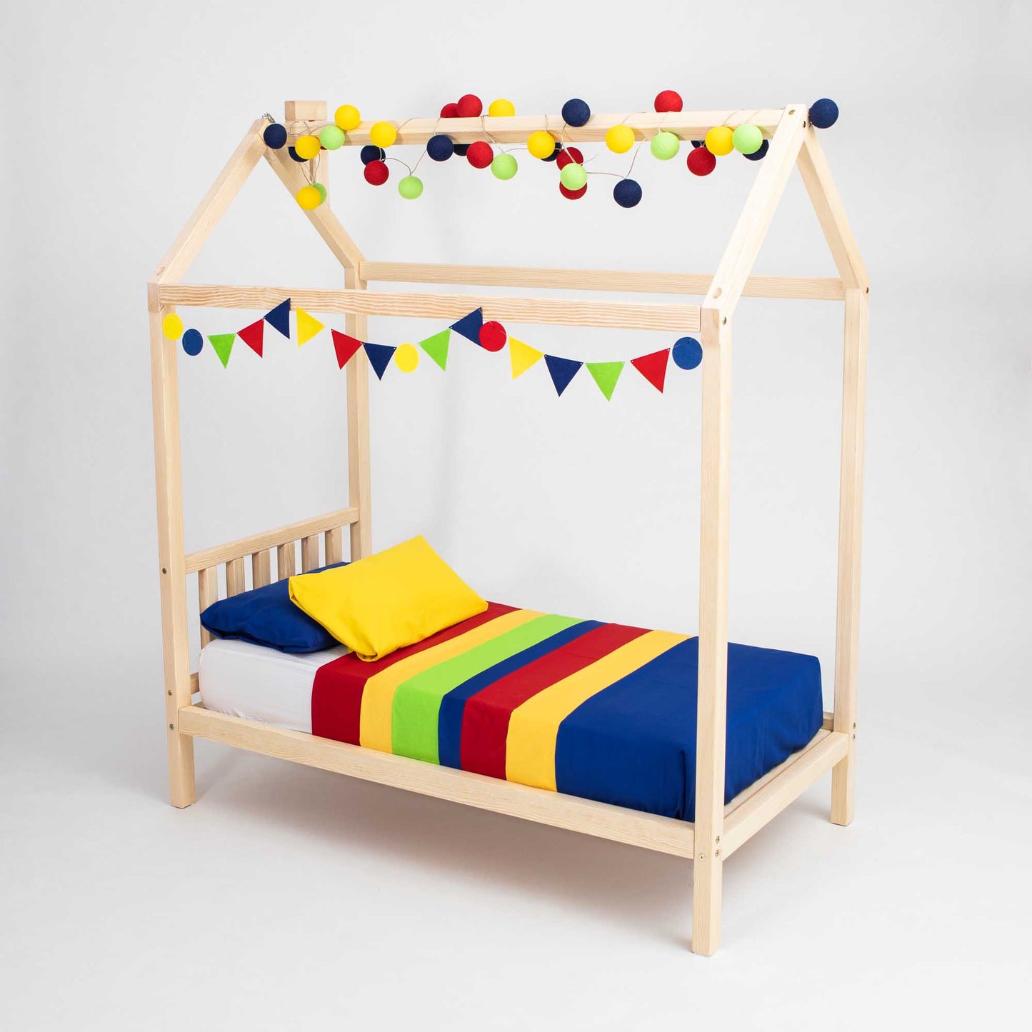 A child's bed with a wooden frame shaped like a house, decorated with colorful bunting and ball lights. This adorable Toddlers' House Bed on Legs with a Headboard includes a multicolored striped blanket and a yellow pillow, creating the perfect kids' sleeping space.