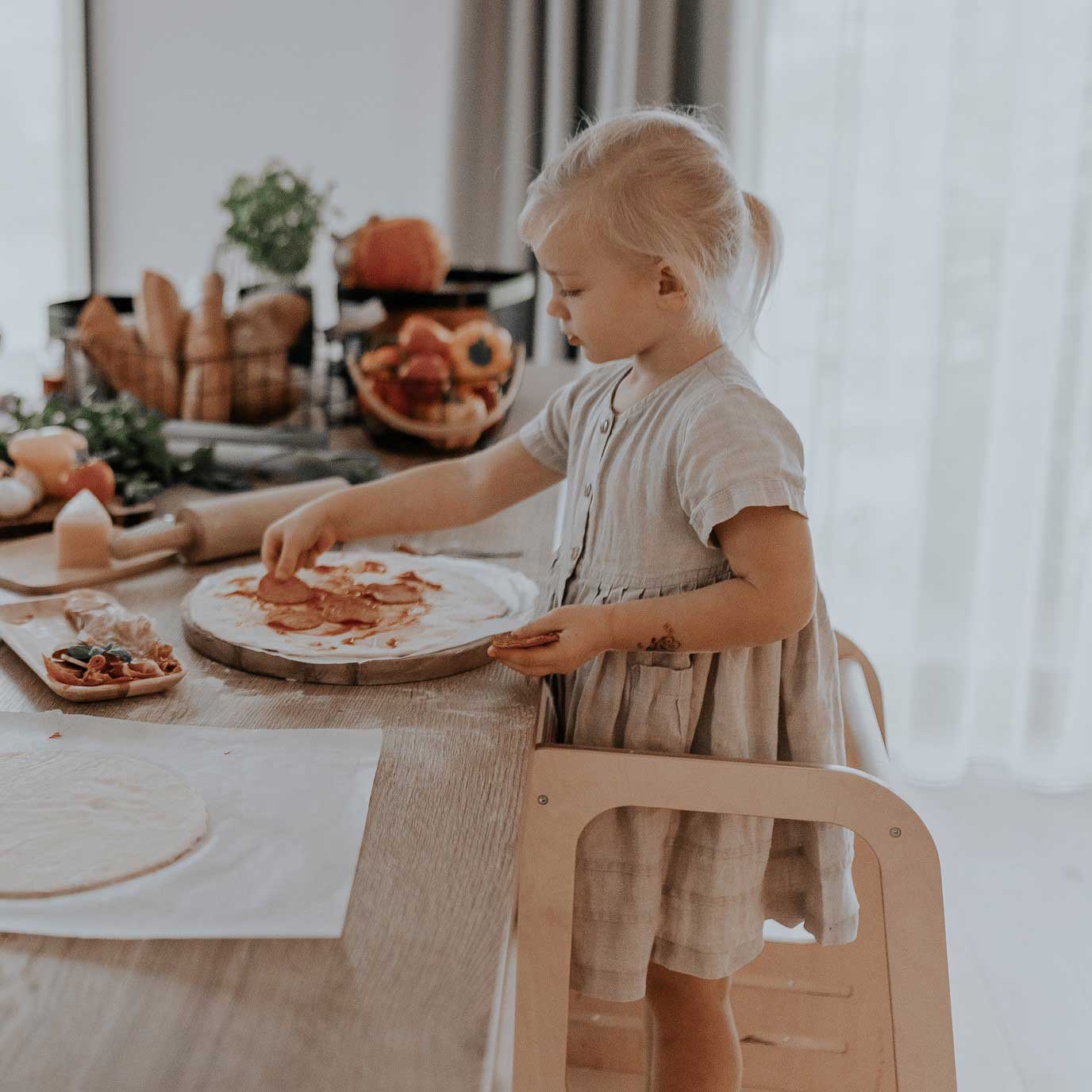 A little girl is making pizza in the kitchen.