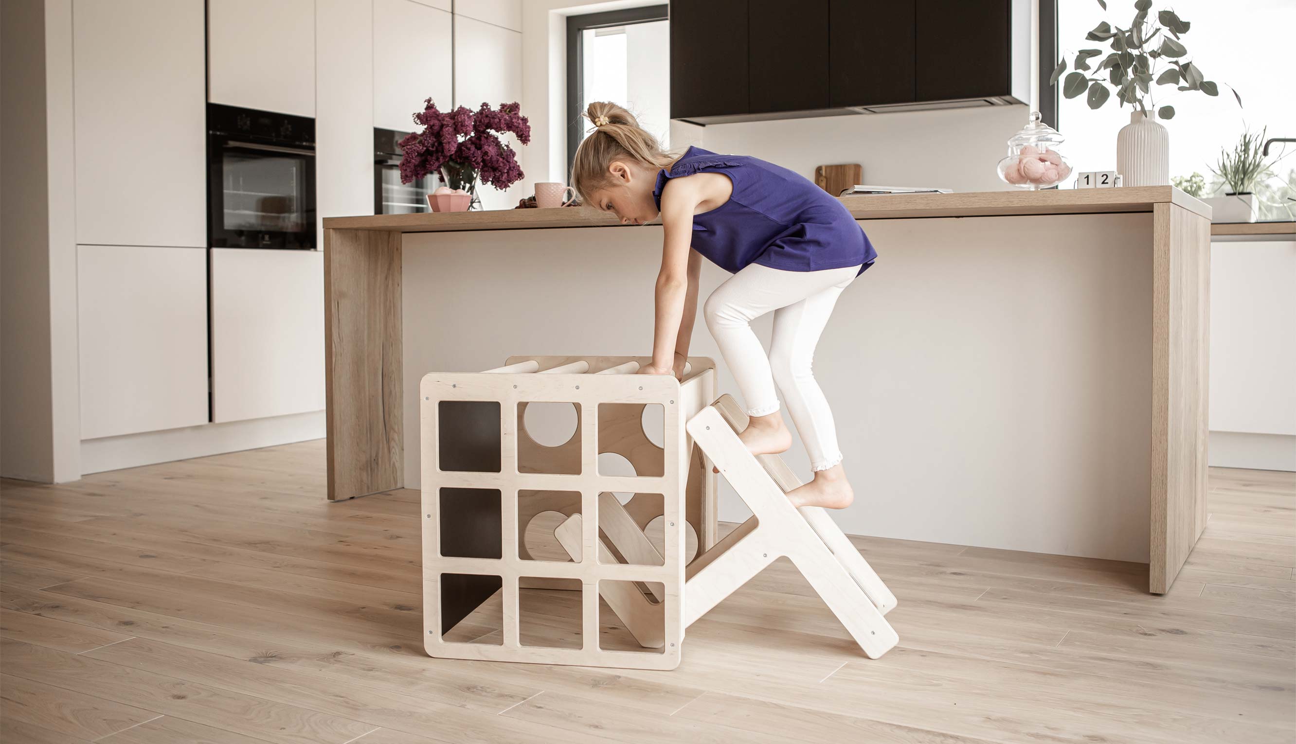 A little girl climbing on a wooden ladder in a kitchen.