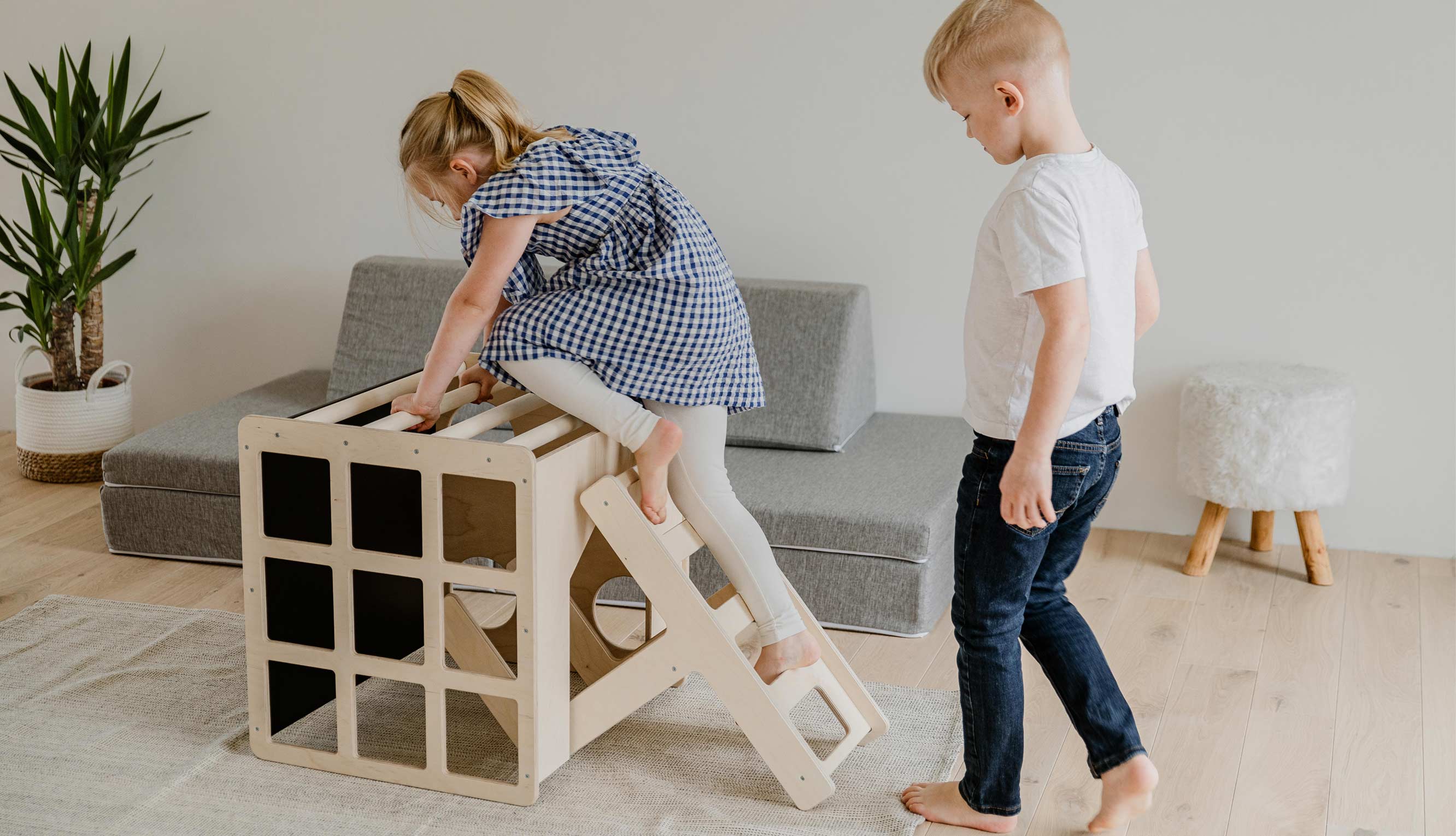 Two children playing with a wooden toy house in a living room.