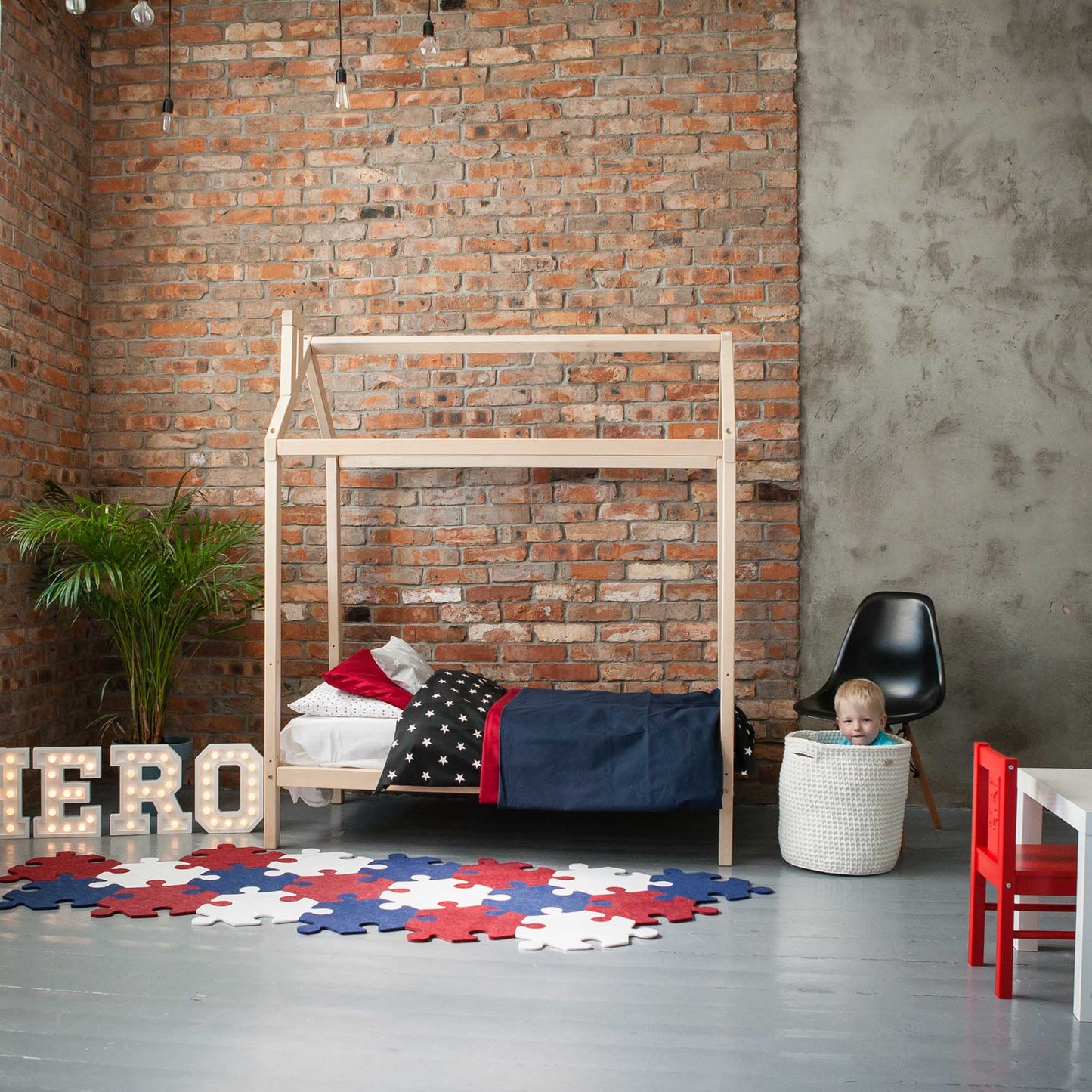 A boy's room with a wooden house bed on legs and a brick wall.