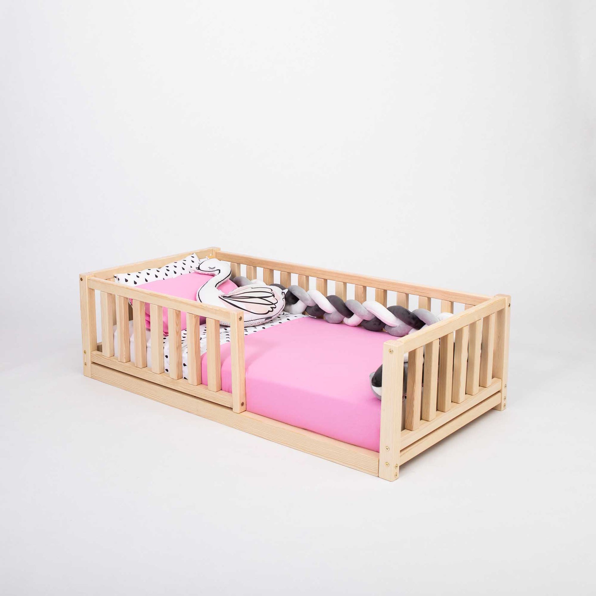 A Sweet Home From Wood 2-in-1 toddler bed on legs with a vertical rail fence and a pink sheet.