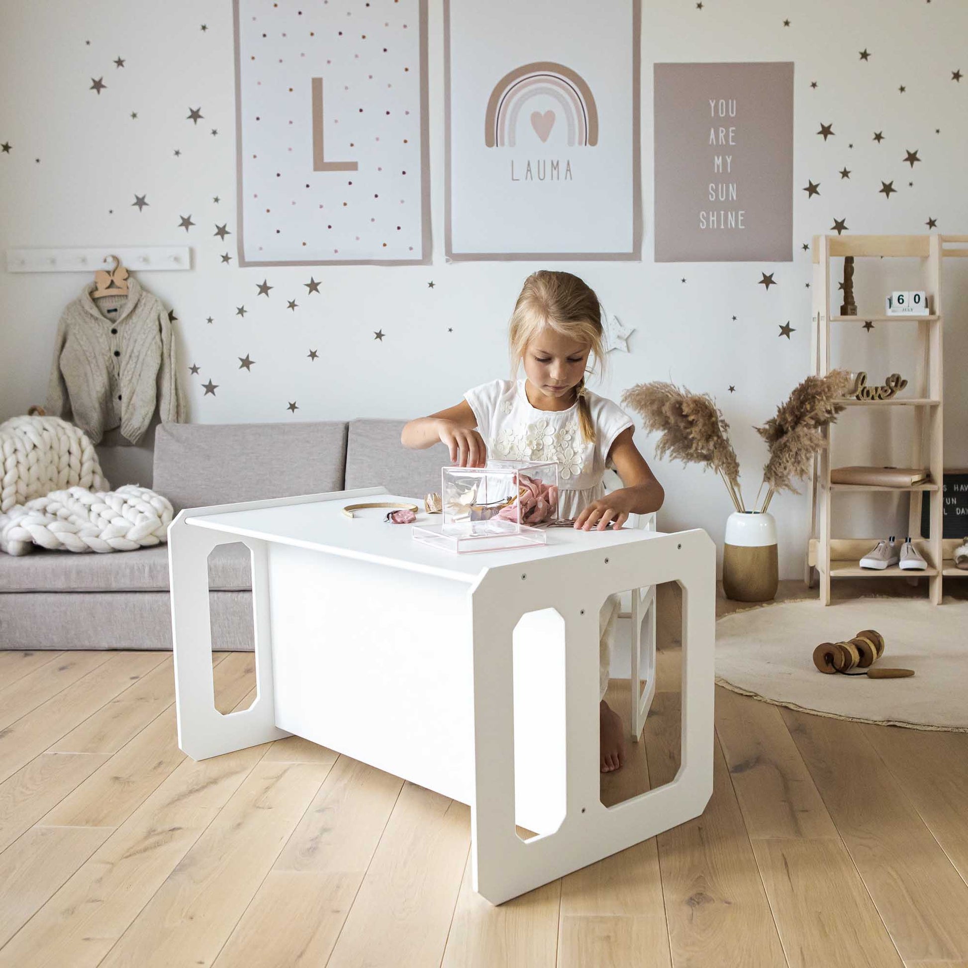 A little girl playing with a Sweet Home From Wood Montessori weaning table and chair set in a living room.