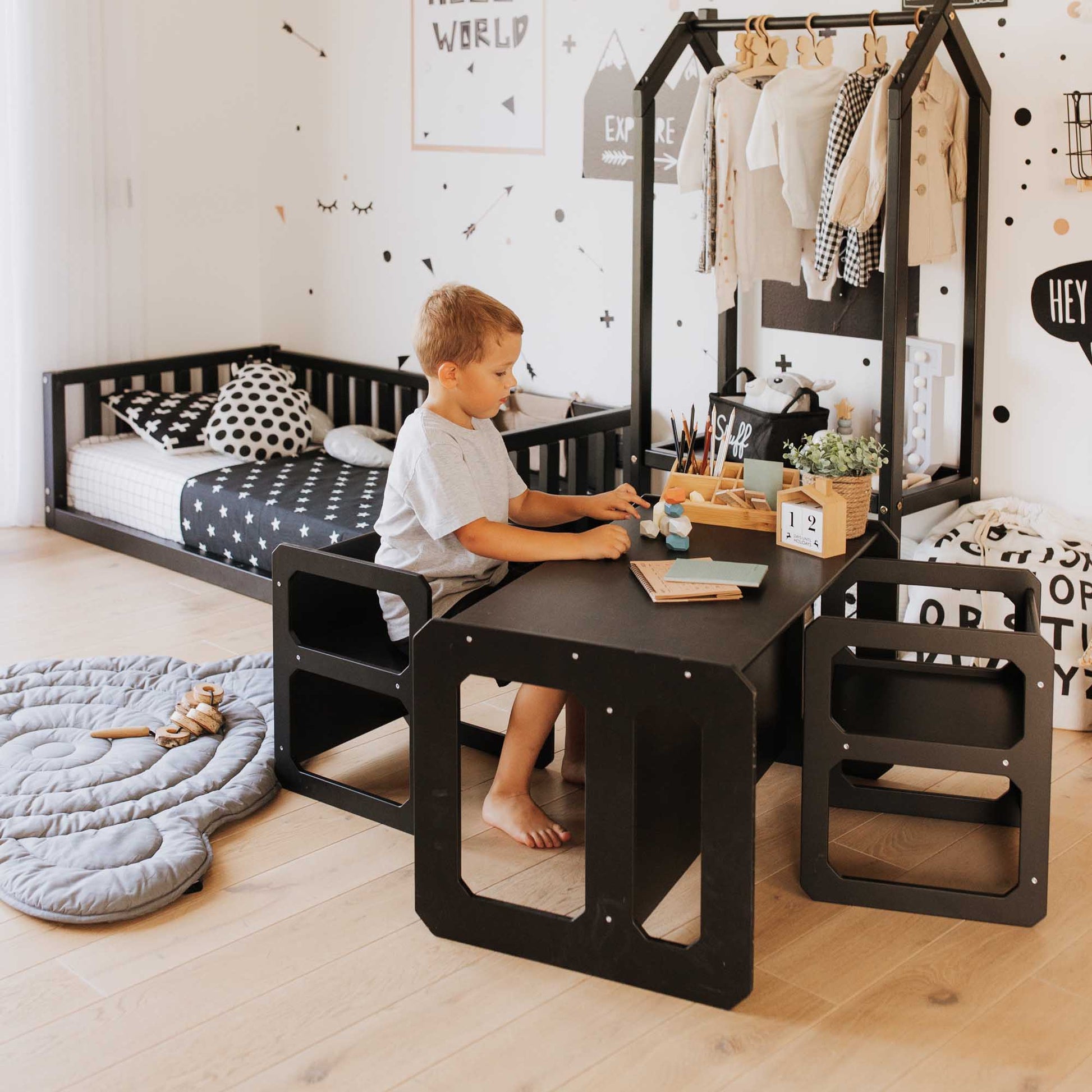 A boy sits independently at a Montessori weaning table and 2 chair set in his room.