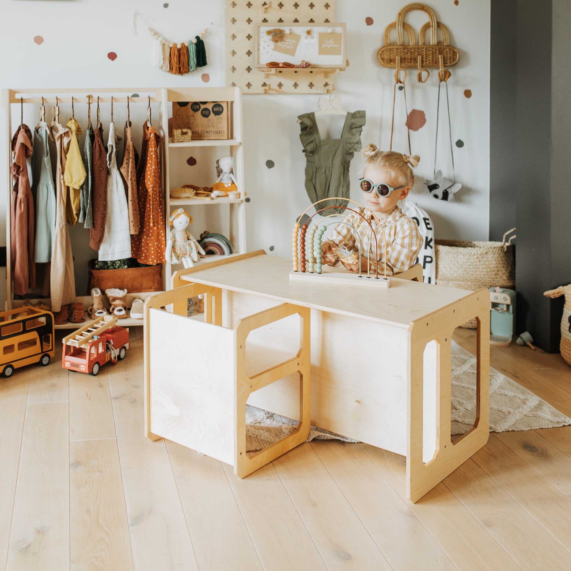 A child sits at a Montessori weaning table and 2 chair set from Sweet Home From Wood in a child's room.