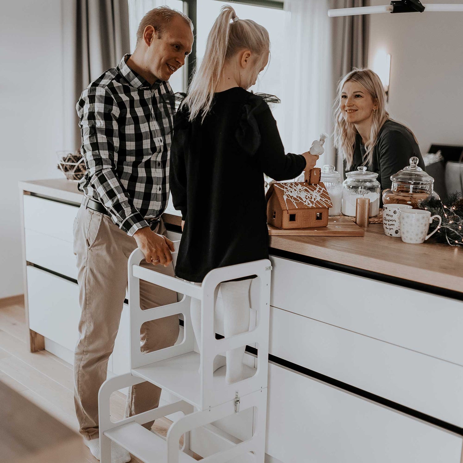 A man and woman standing in front of a kitchen with a child on a step stool.