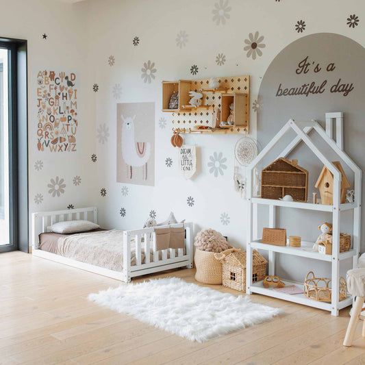 A child's bedroom showcases a kids' bed with a headboard and footboard, shelves shaped like a house, wall decor including an alphabet chart, and various toys. The room has a white rug and wall art saying "It's a beautiful day.