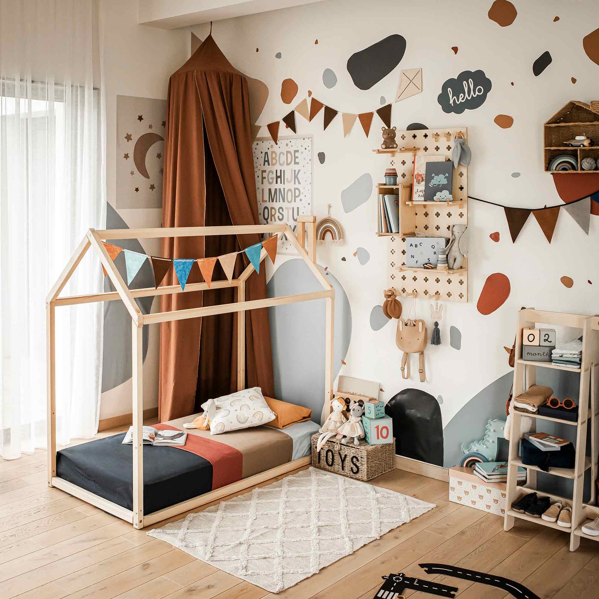 Children's room with a Wooden Zero-Clearance House Bed, decorative bunting, bookshelves, stuffed toys, and educational wall decor. The room has light wood flooring and playful wall art.