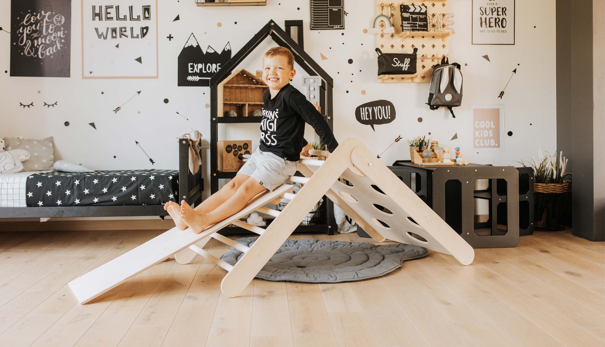 A boy is playing with a wooden slide in his room.