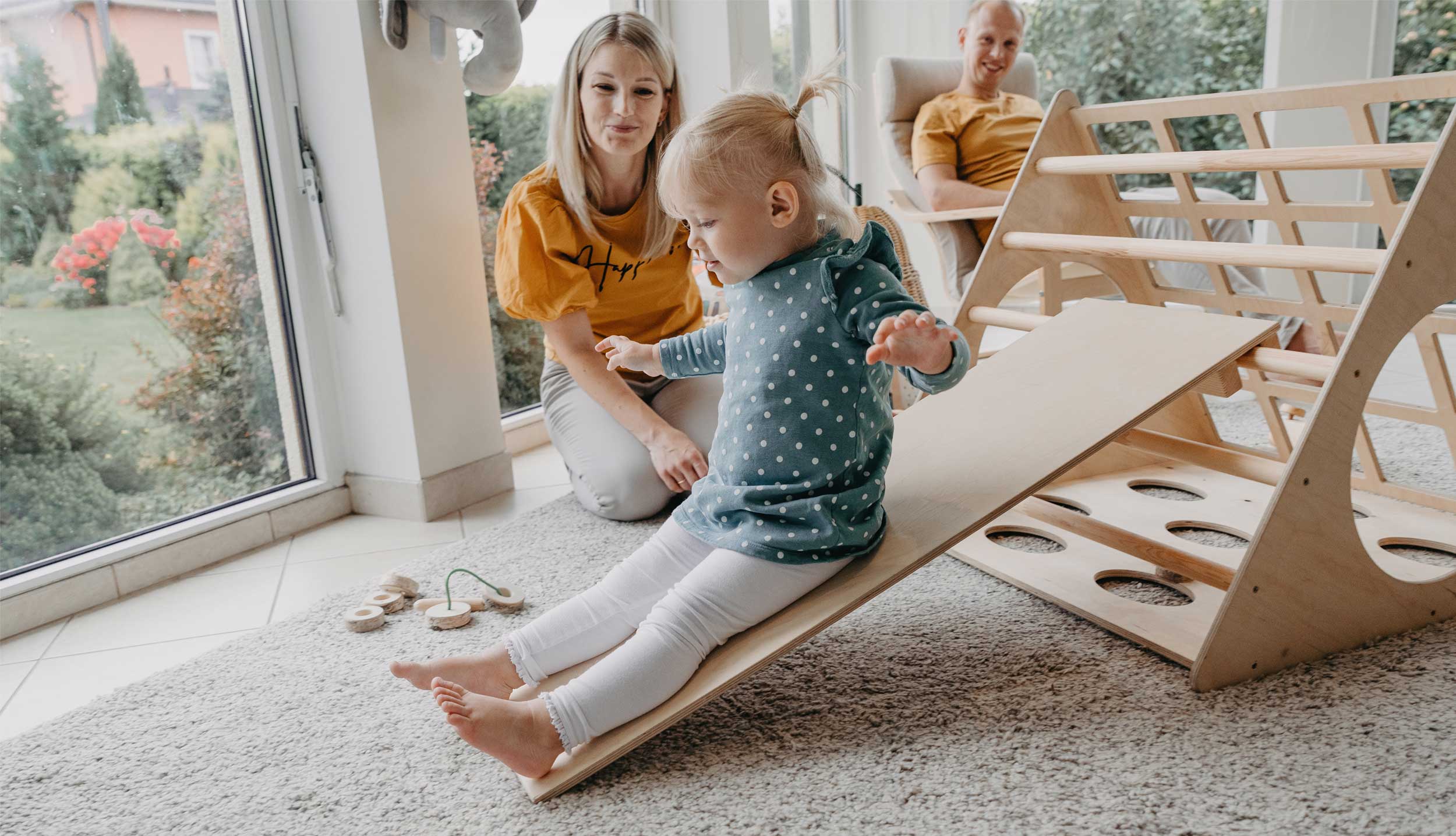 A child playing with a wooden slide in a living room.