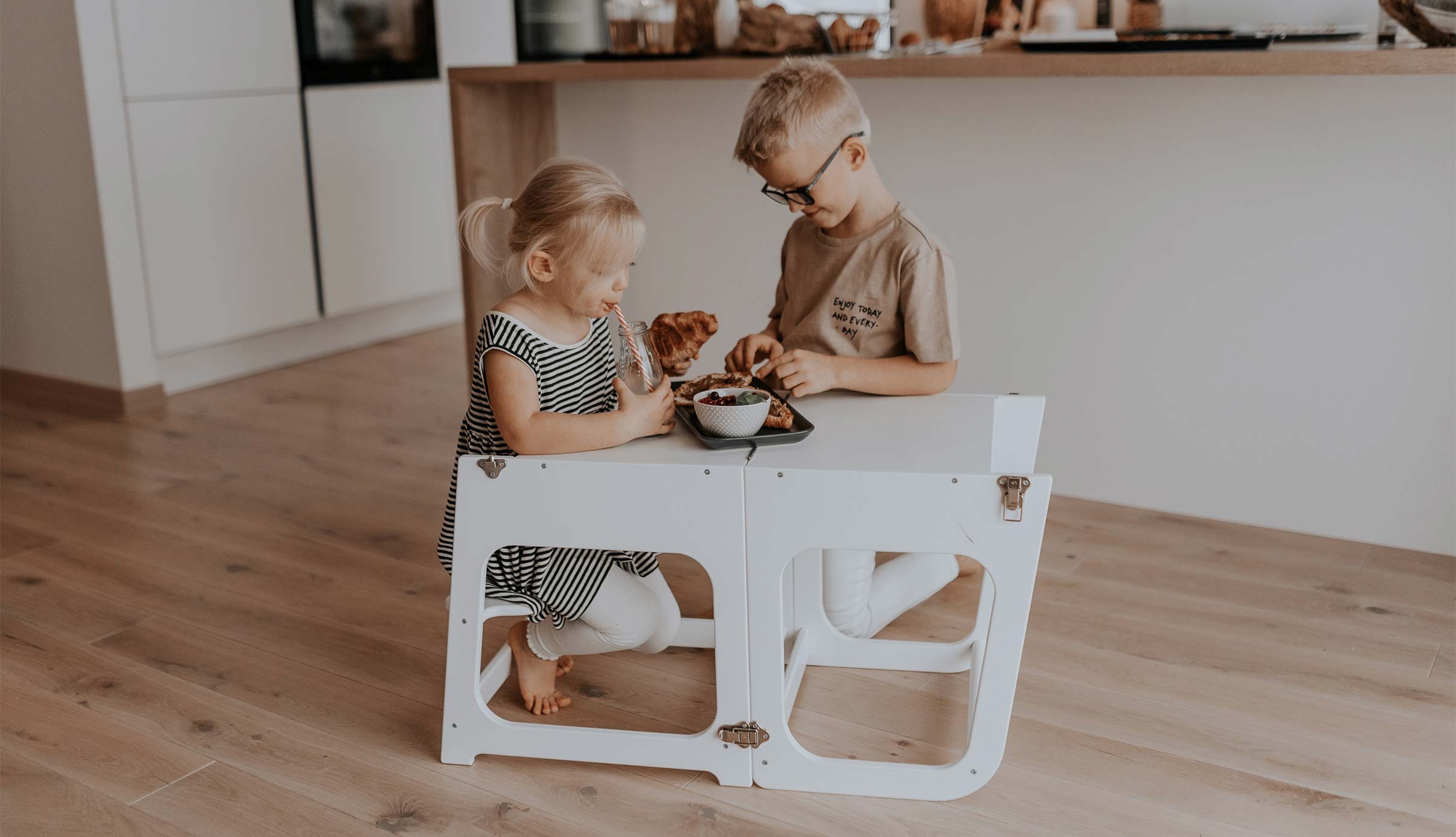 Two children sitting at a table in a kitchen.