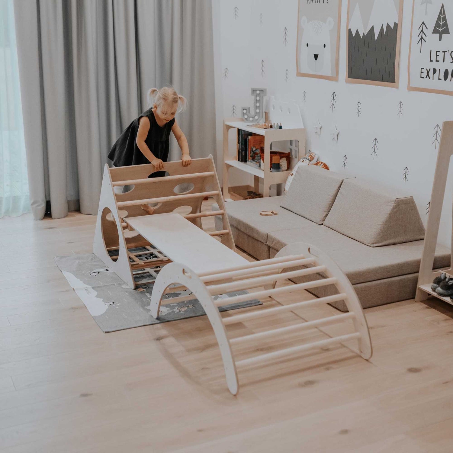 A child is playing with a Sweet Home From Wood wooden climbing triangle, climbing arch, and ramp in a room.