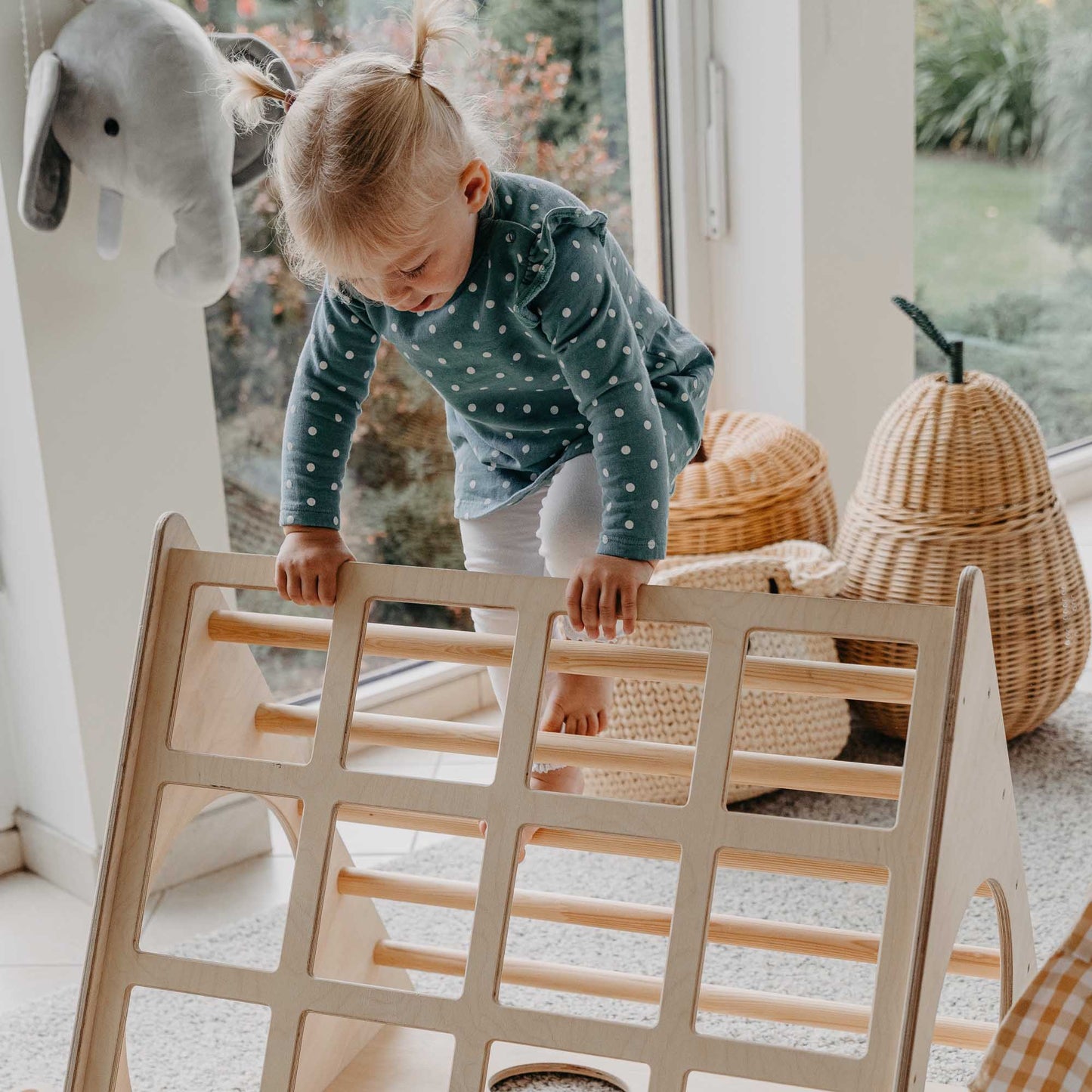 A little girl playing with a climbing triangle with sensory panels in a living room.