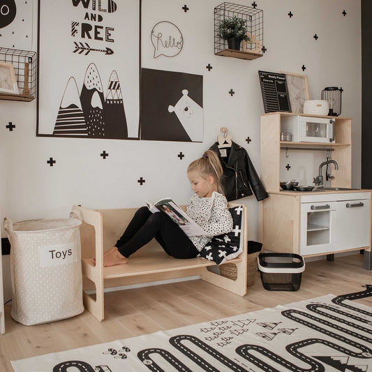 A black and white playroom with a little girl reading a book at a Sweet Home From Wood Montessori weaning table.