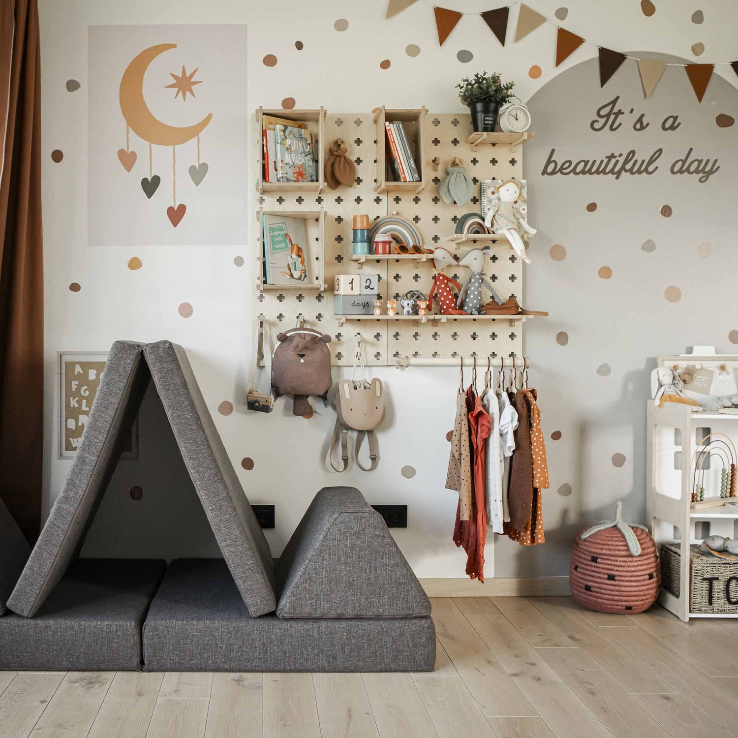 A stylish children's room with a gray play tent, a polka-dotted wall, a Large Pegboard Shelf with Clothing Rack holding toys, hanging clothes, and a sign that says "It's a beautiful day." The decor includes a moon and stars mobile.