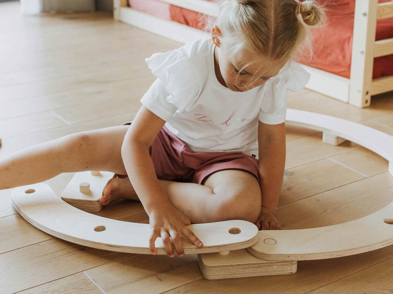 A little girl playing with a wooden toy on the floor.