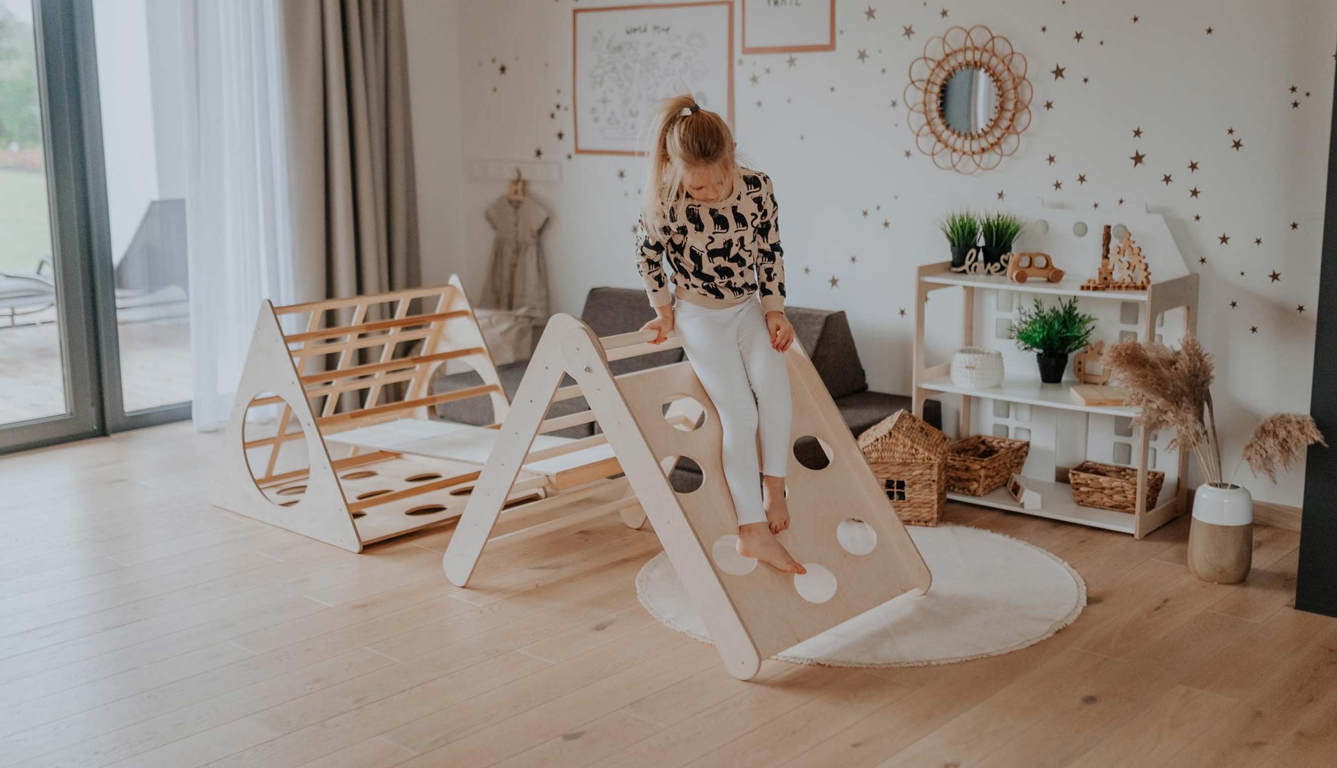 A girl standing in a room with a wooden play structure.