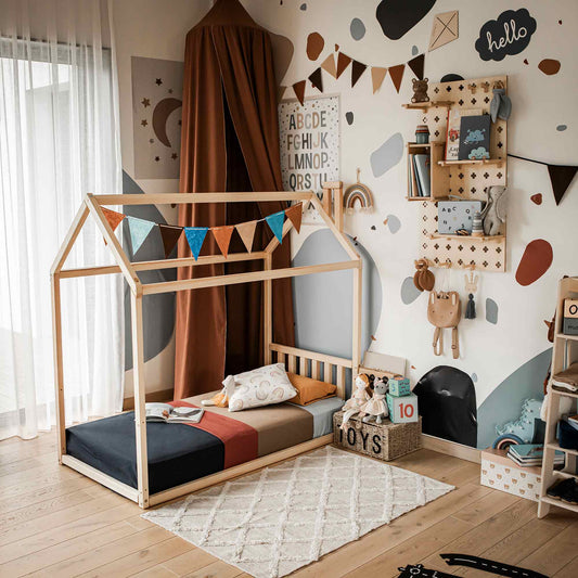 A children's room features a House-frame bed with a headboard adorned with colorful buntings, a rug, a bookshelf, and various toys. The walls display playful decorations, including a banner and wall-mounted items, ensuring a secure and snug night's sleep.