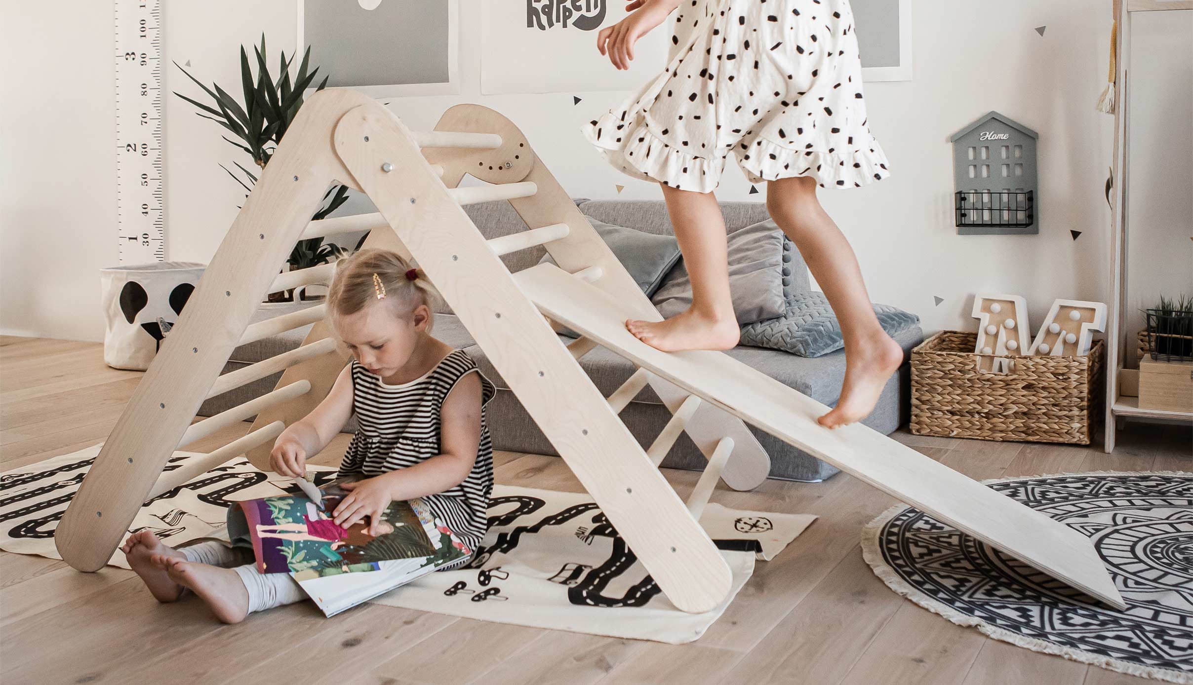 A girl is playing with a wooden slide in her living room.