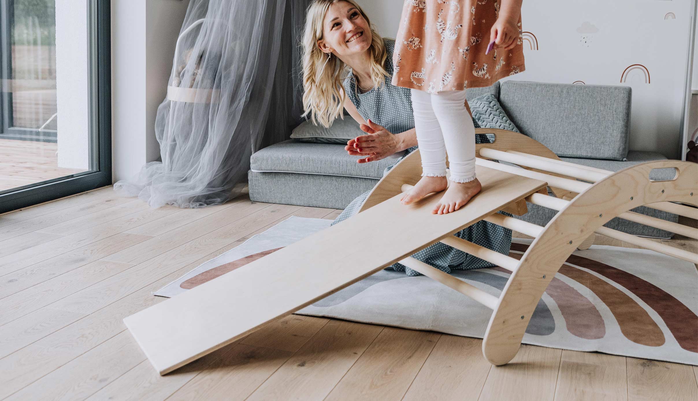 A mother and daughter playing on a wooden slide in a living room.