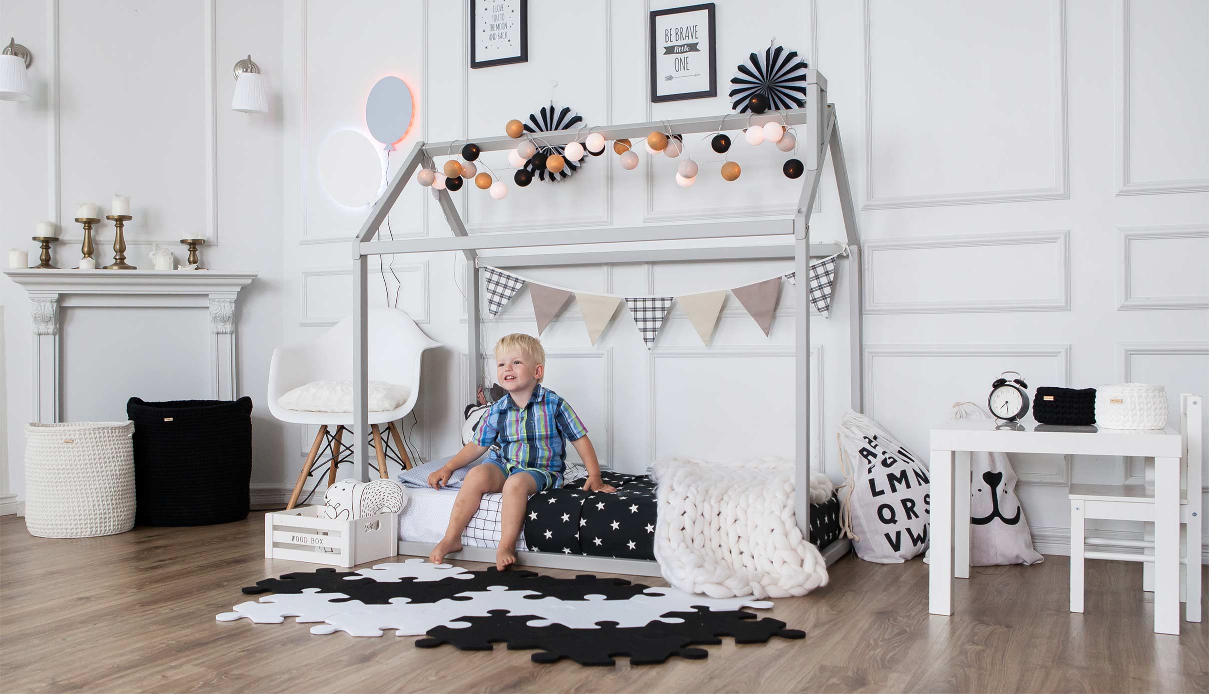 A little boy sits on a bed in a black and white room.